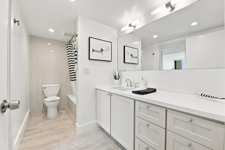 Bathroom featuring a single vanity with ample counter space, white cabinetry, a built-in shower/tub combination, and neutral-toned tile flooring