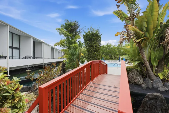 Vibrant red pedestrian bridge over a water feature, bordered by lush tropical landscaping