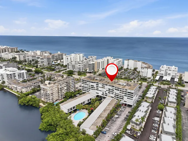 Ocean to Intracoastal multi-story building featuring a white exterior with horizontal architectural elements, surrounded by extensive parking areas, mature landscaping, and a nearby water body