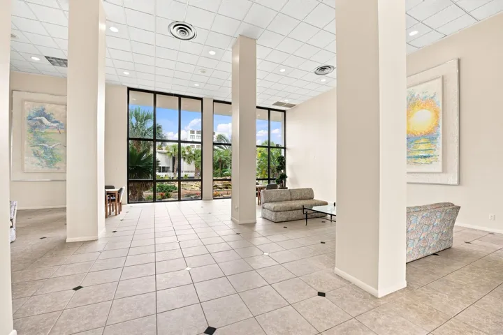 Spacious ground floor lobby greets you featuring light-toned tile flooring with dark accent inlays, multiple structural columns, and large floor-to-ceiling windows