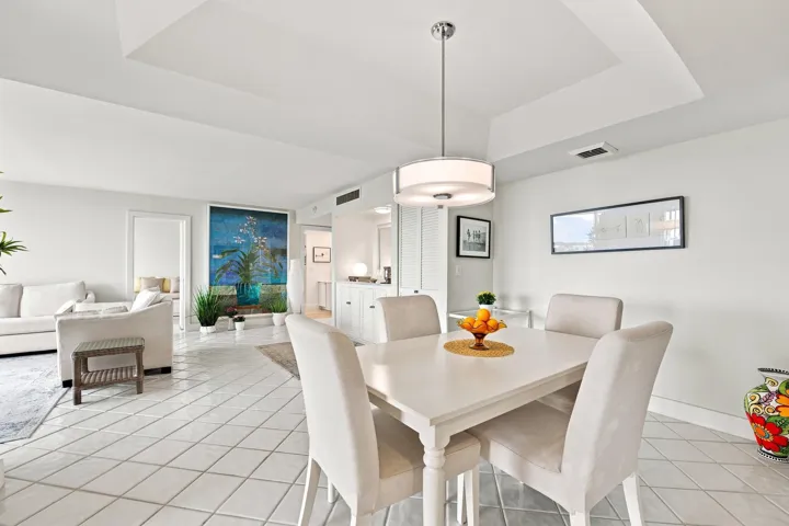 Open concept living and dining area featuring large format diagonal tile flooring, a tray ceiling, and a modern drum pendant light fixture