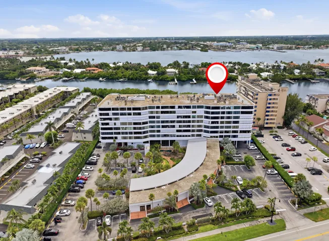 Waterfront high-rise building featuring multiple levels of balconies, extensive on-site parking, a curved entry drive, and mature landscaping