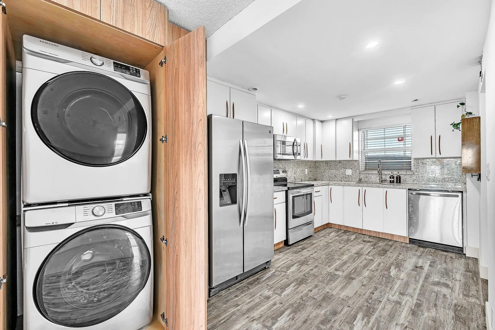 White cabinetry with coordinating hardware, stainless steel appliances, wood-finish flooring, and a stacked washer and dryer