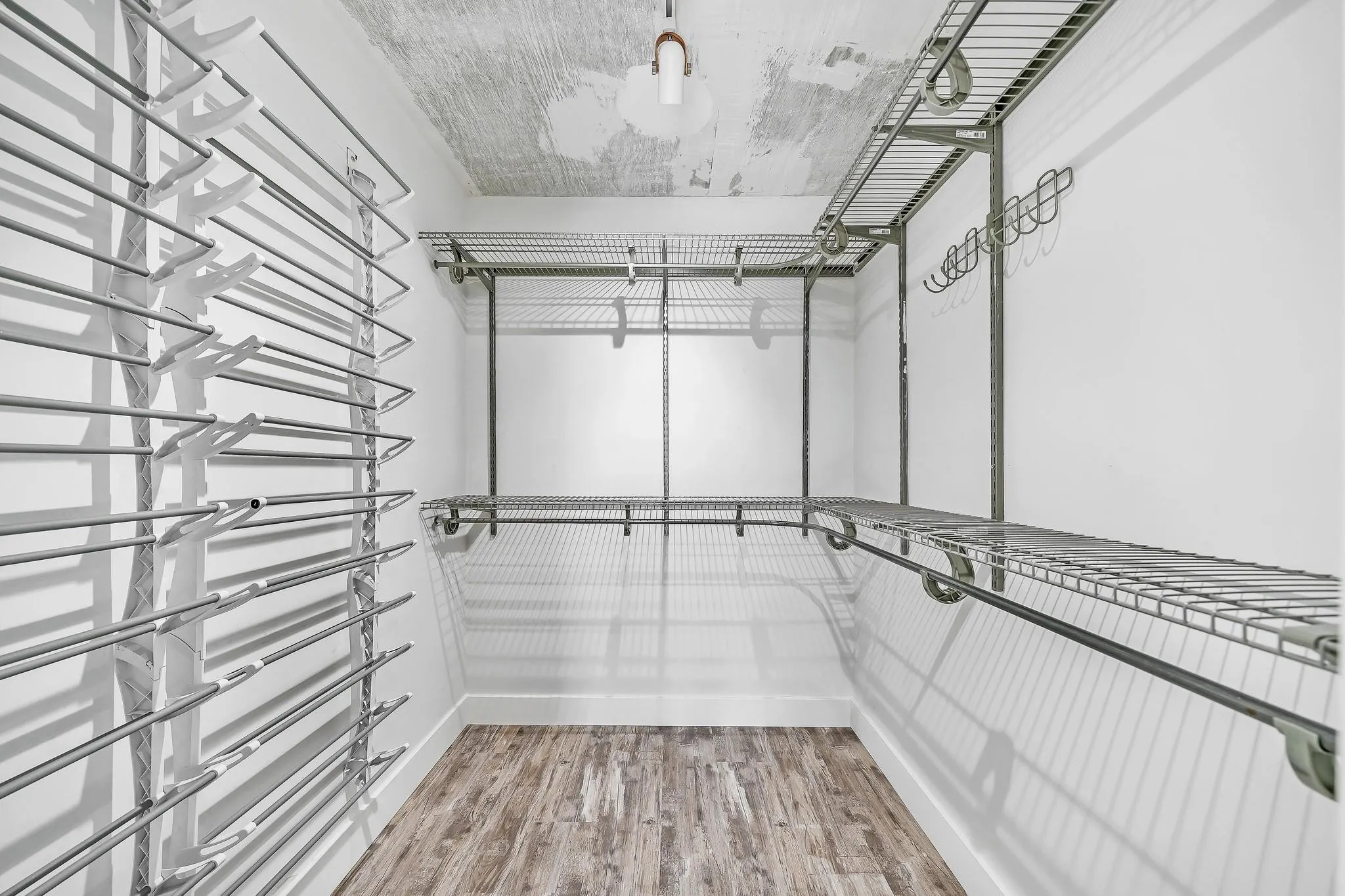 Walk-in closet featuring wood-finish flooring, white walls, built-in wire shelving, and multiple hanging rods