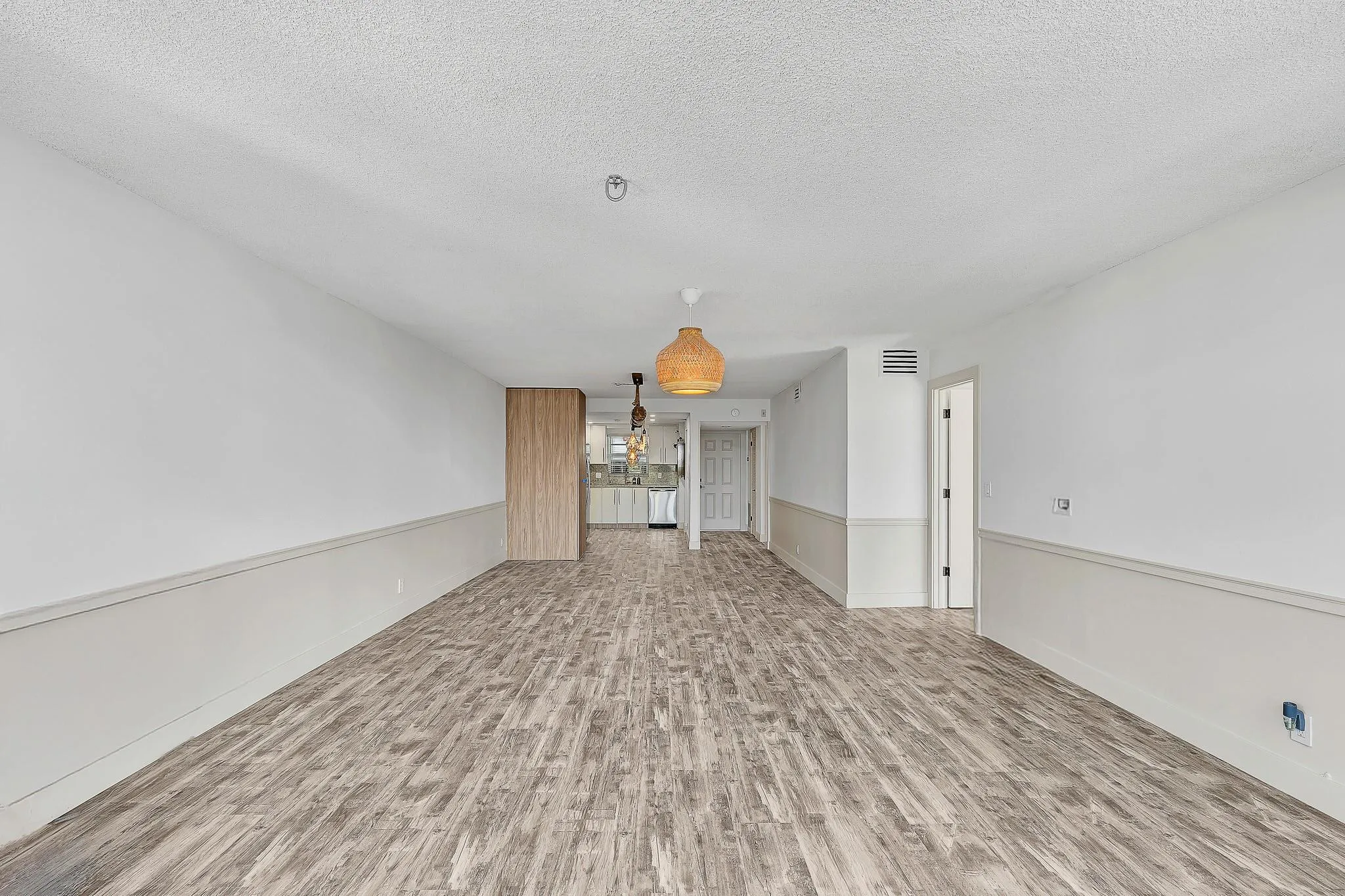 Wood-finish flooring throughout, white walls with half-wall paneling, and two woven pendant light fixtures