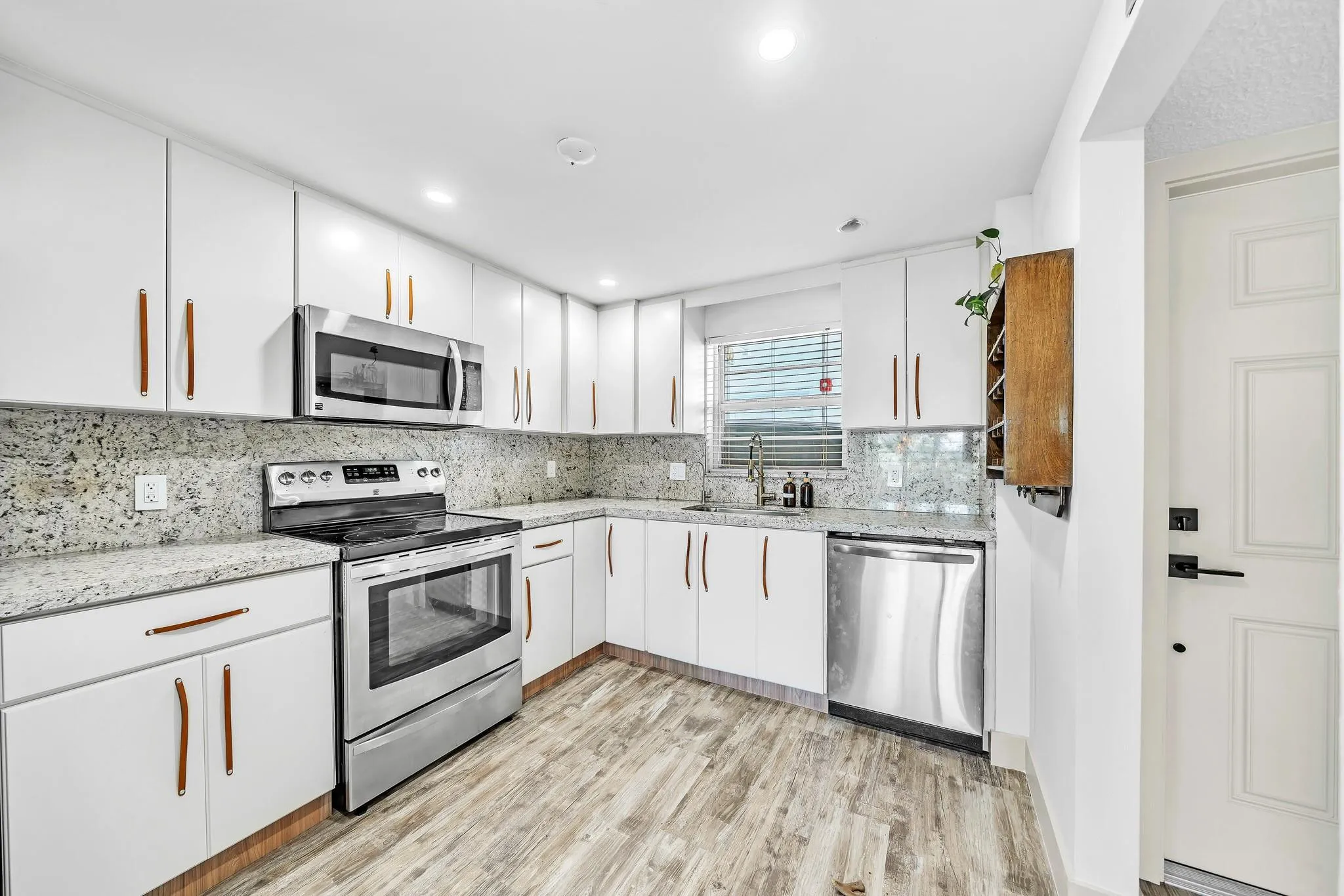 Updated kitchen with white cabinetry, stainless steel appliances, speckled countertops, and wood-finish flooring