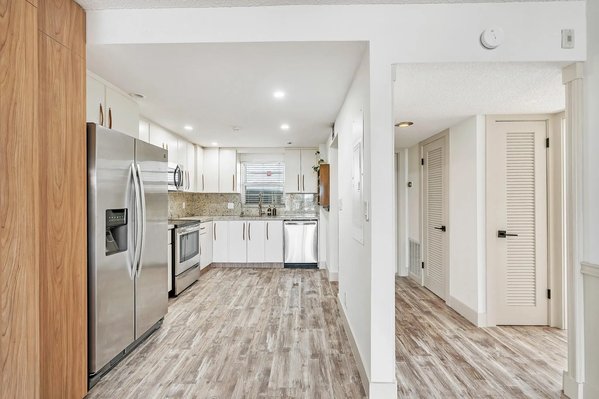 Kitchen featuring white cabinetry, stainless steel appliances, granite countertops, and wood-finish flooring