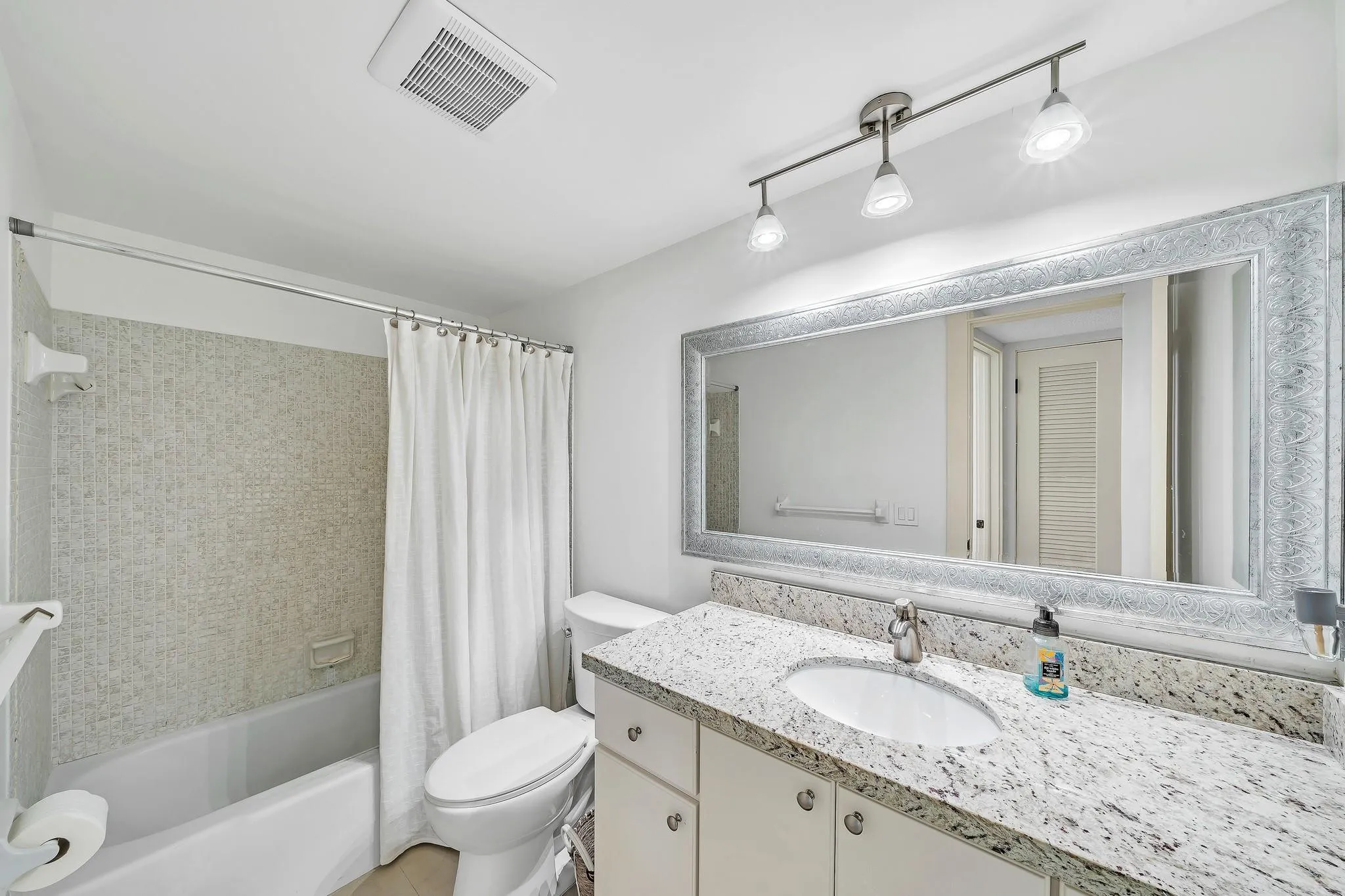 Bathroom featuring a vanity with a white-finish cabinet, stone-finish countertop, single basin sink, and framed mirror, along with a tub and shower combination with tile surround