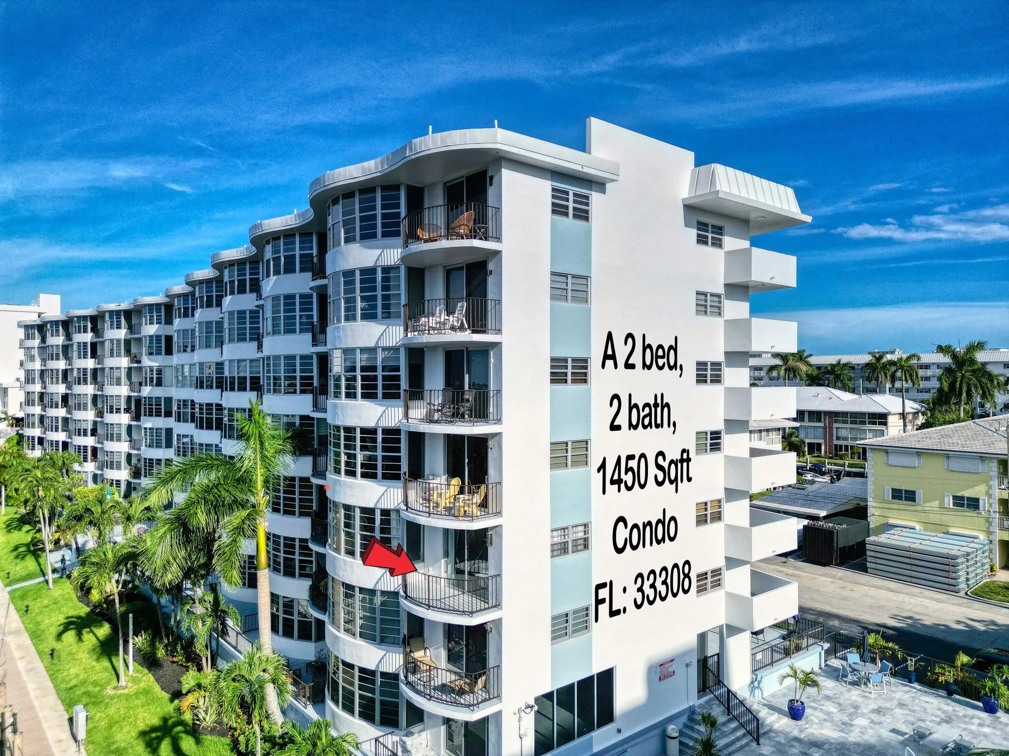 Mid-rise residential building featuring multiple balconies, extensive window-lined facades, and mature palm trees