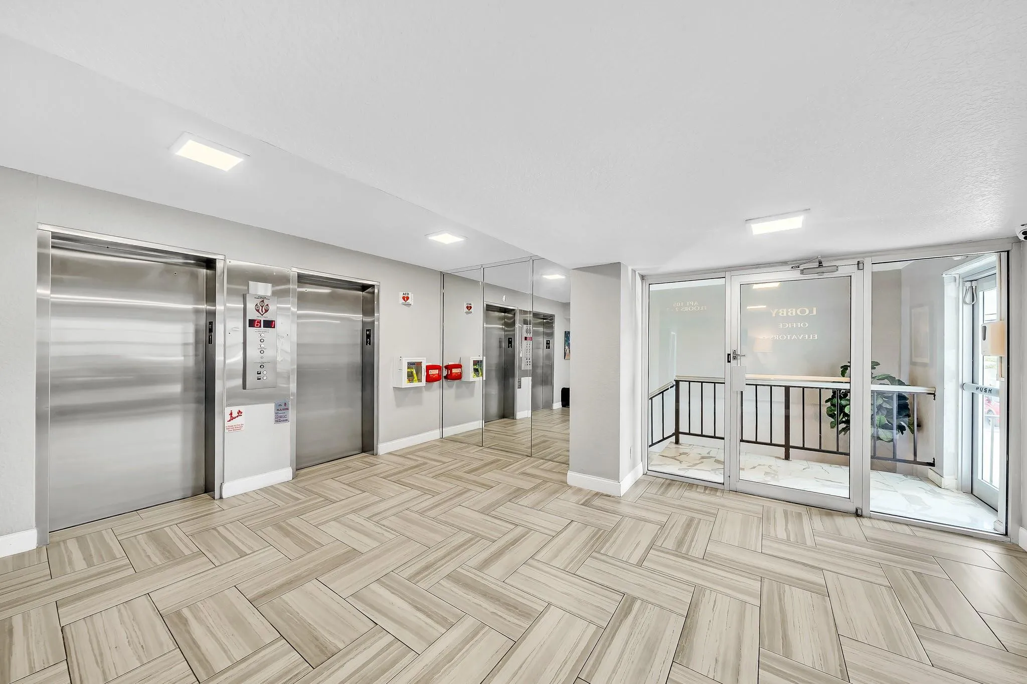 Lobby with patterned tile flooring, two stainless steel elevators, mirrored wall accents, and glass-paneled entry doors