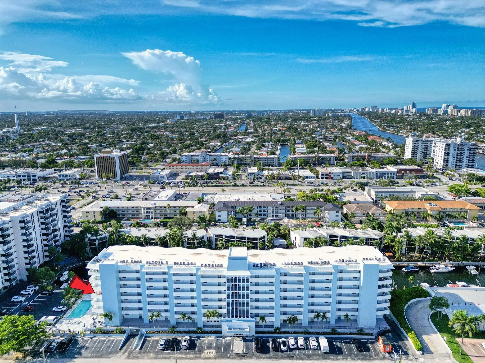 Multi-story building featuring multiple balconies, ground-level parking, and a swimming pool with surrounding deck