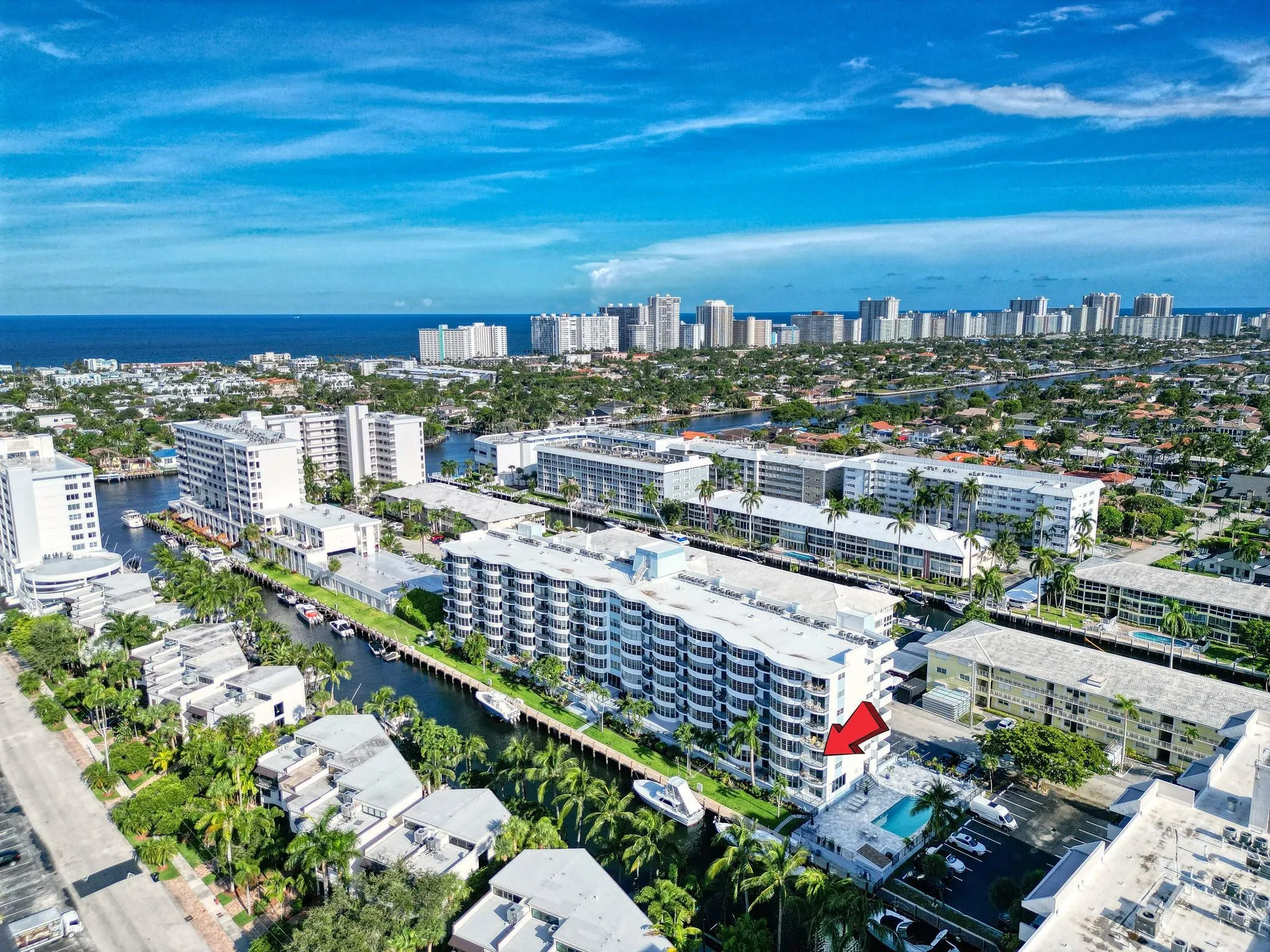 Multistory residential building featuring multiple balconies, a ground-level pool, and surrounding waterways