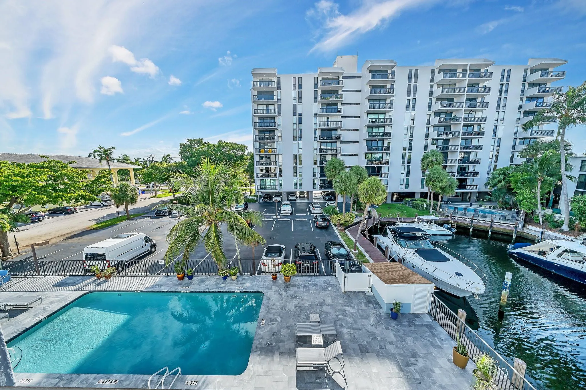 Outdoor swimming pool with a paved deck, directly adjacent to a waterway with boat docks
