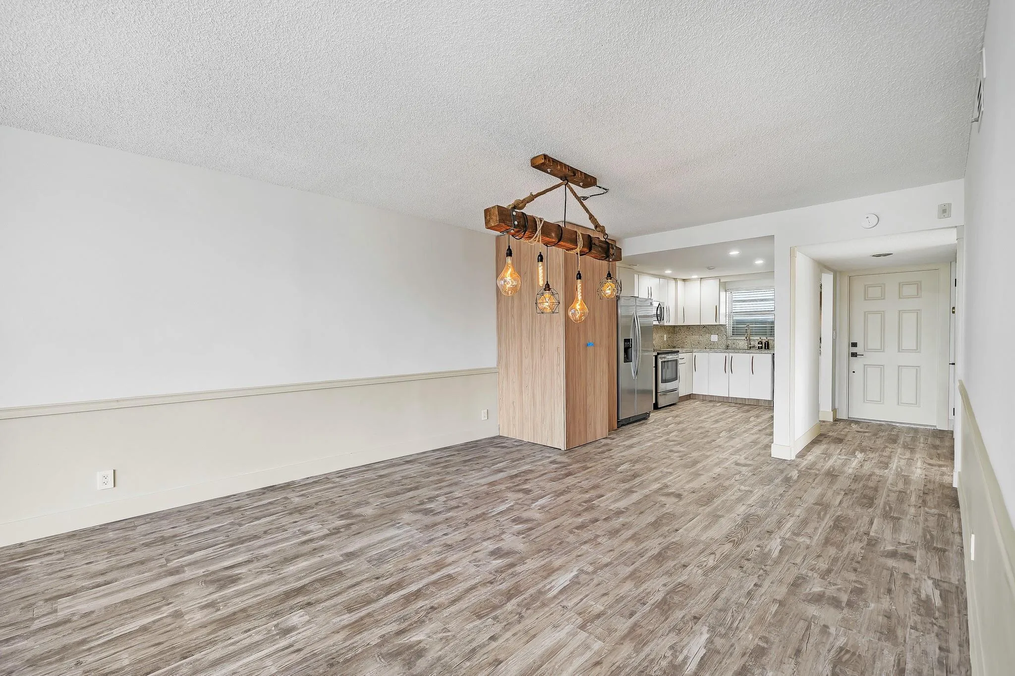 Wood-finish flooring throughout, with a recessed kitchen featuring white cabinetry, stainless steel appliances, and a tiled backsplash