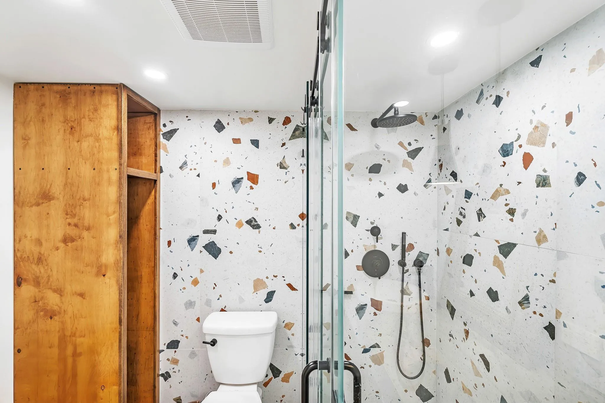 Glass-enclosed shower with matte black fixtures, rain shower head, and colorful terrazzo-style tile