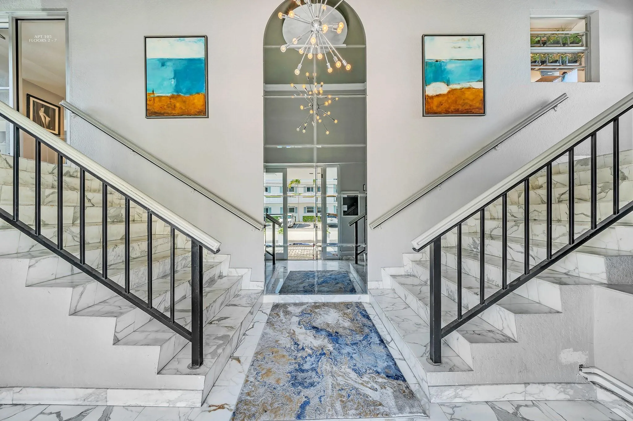 Grand entryway featuring dual staircases, marble-finish flooring, a modern chandelier, an arched ceiling, and abundant natural light