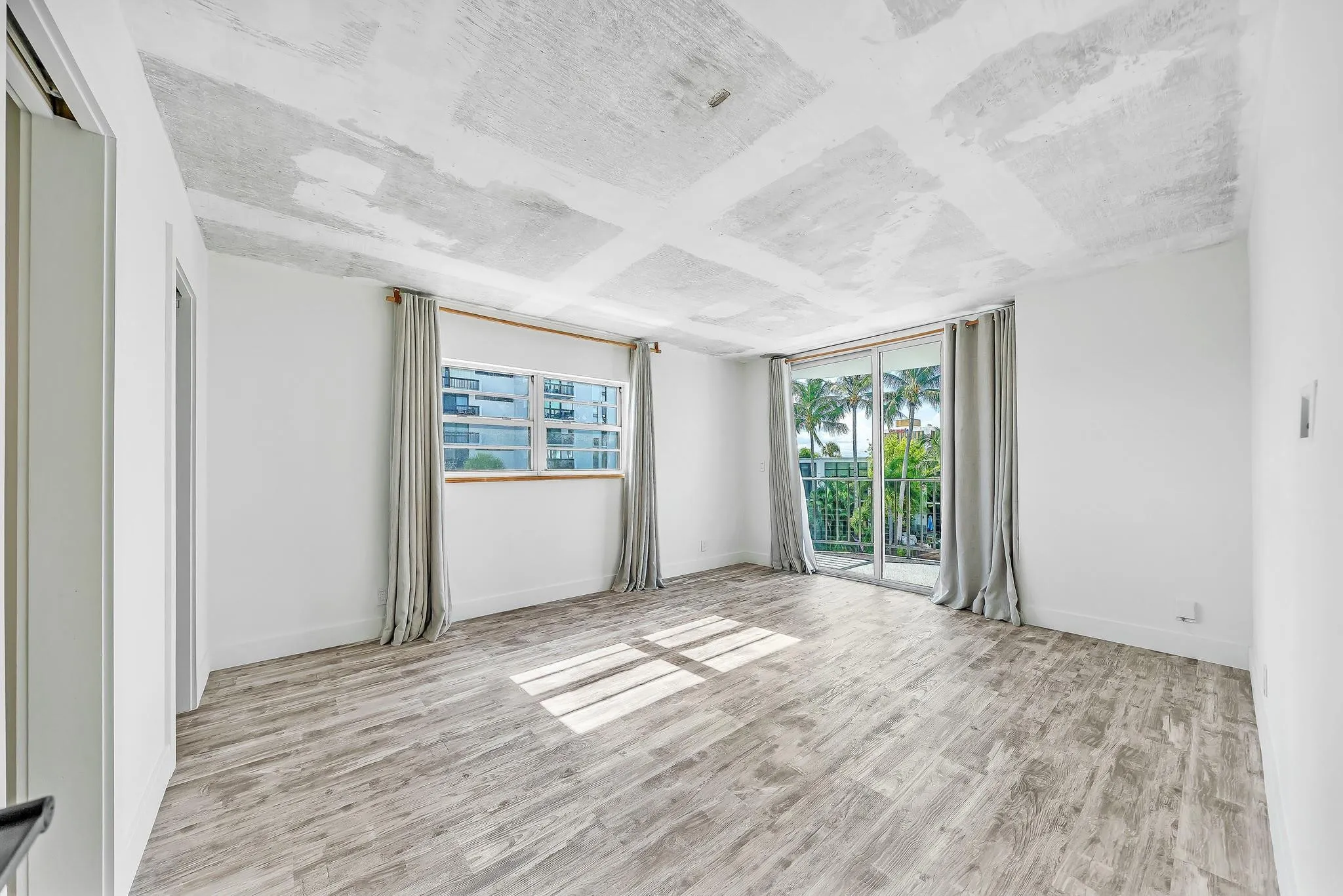 Spacious room featuring wood-finish flooring, white walls, and a large sliding glass door opening to a balcony