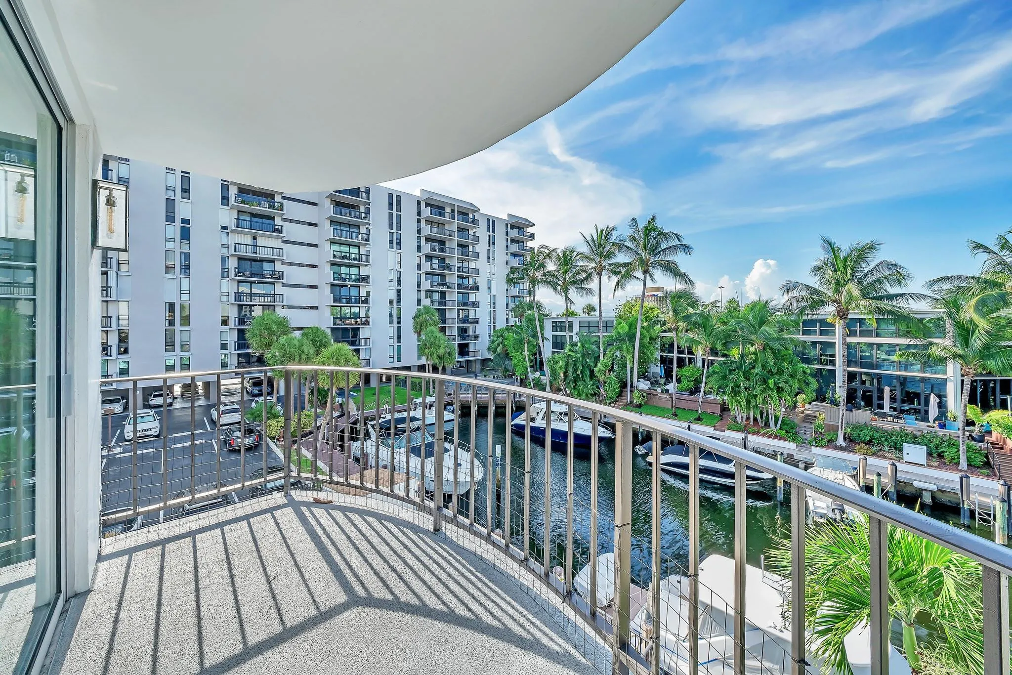 Curved balcony with metal railing overlooking a canal with boats, palm trees, and residential buildings