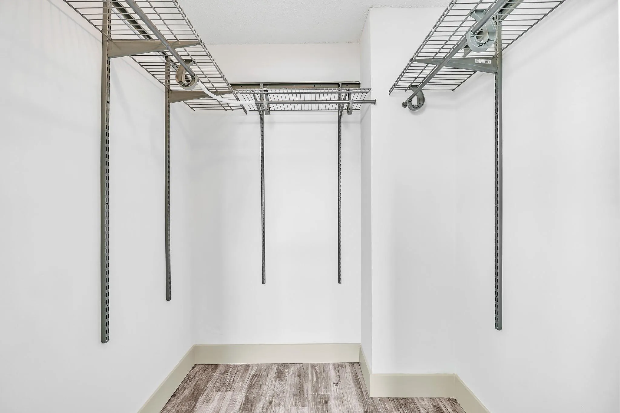 Built-in wire shelving, adjustable hanging rods, white walls, wood-finish flooring, and light-colored baseboards