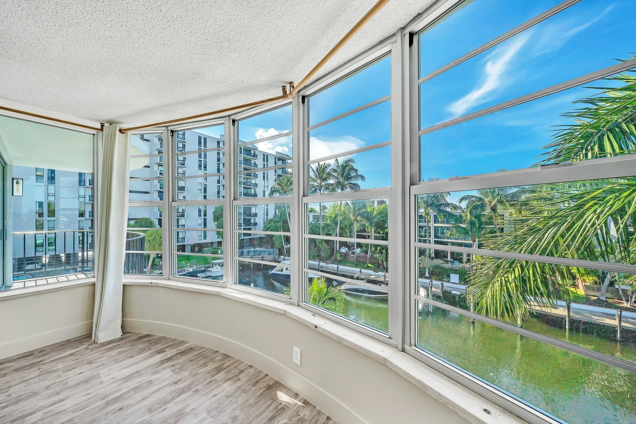 Curved bay window with wood-finish flooring, textured ceilings, and a partial balcony