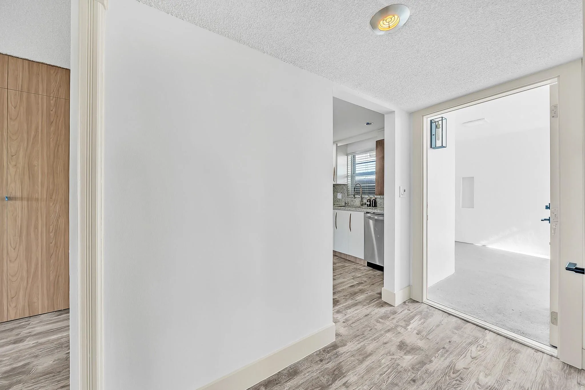 Wood-finish flooring throughout, with a neutral white wall finish and a built-in kitchen featuring stainless steel appliances