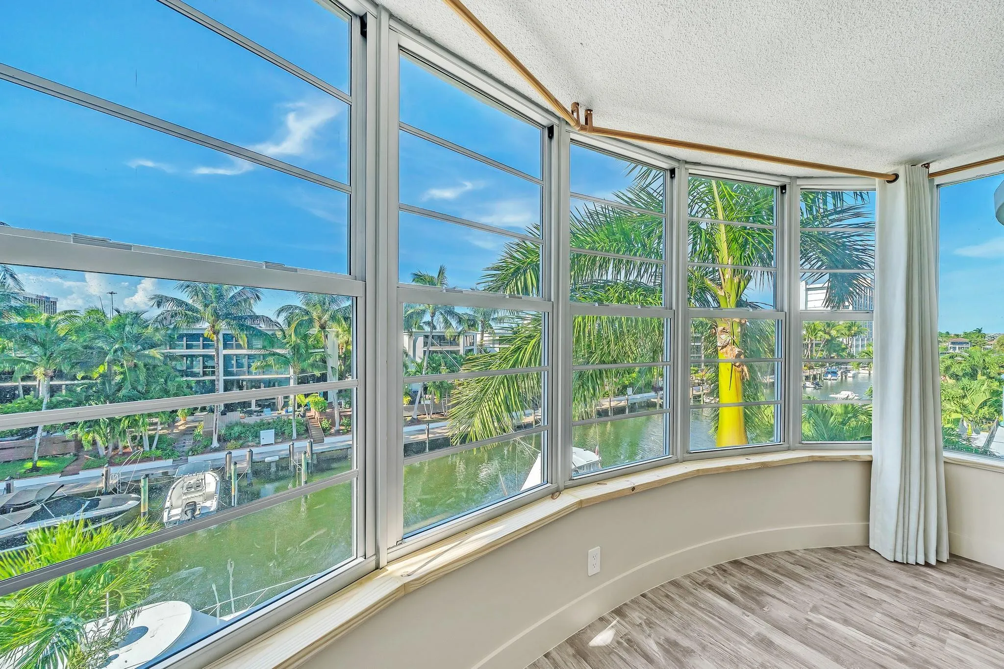 Curved window wall with multiple large pane windows, wood-finish flooring, and a waterway background with boats