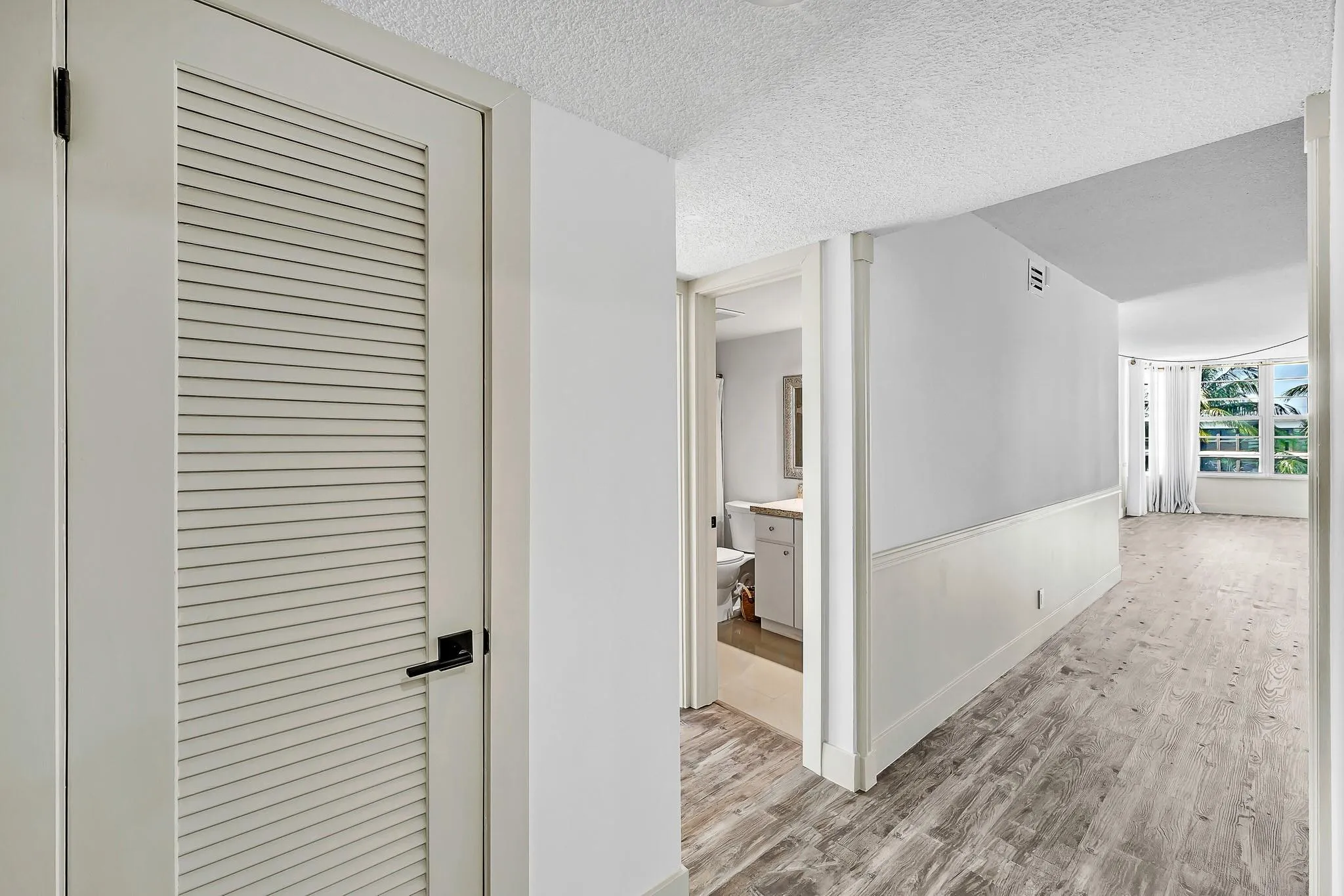 Louvered door with black hardware, wood-finish flooring, half wall with paneling, and large windows