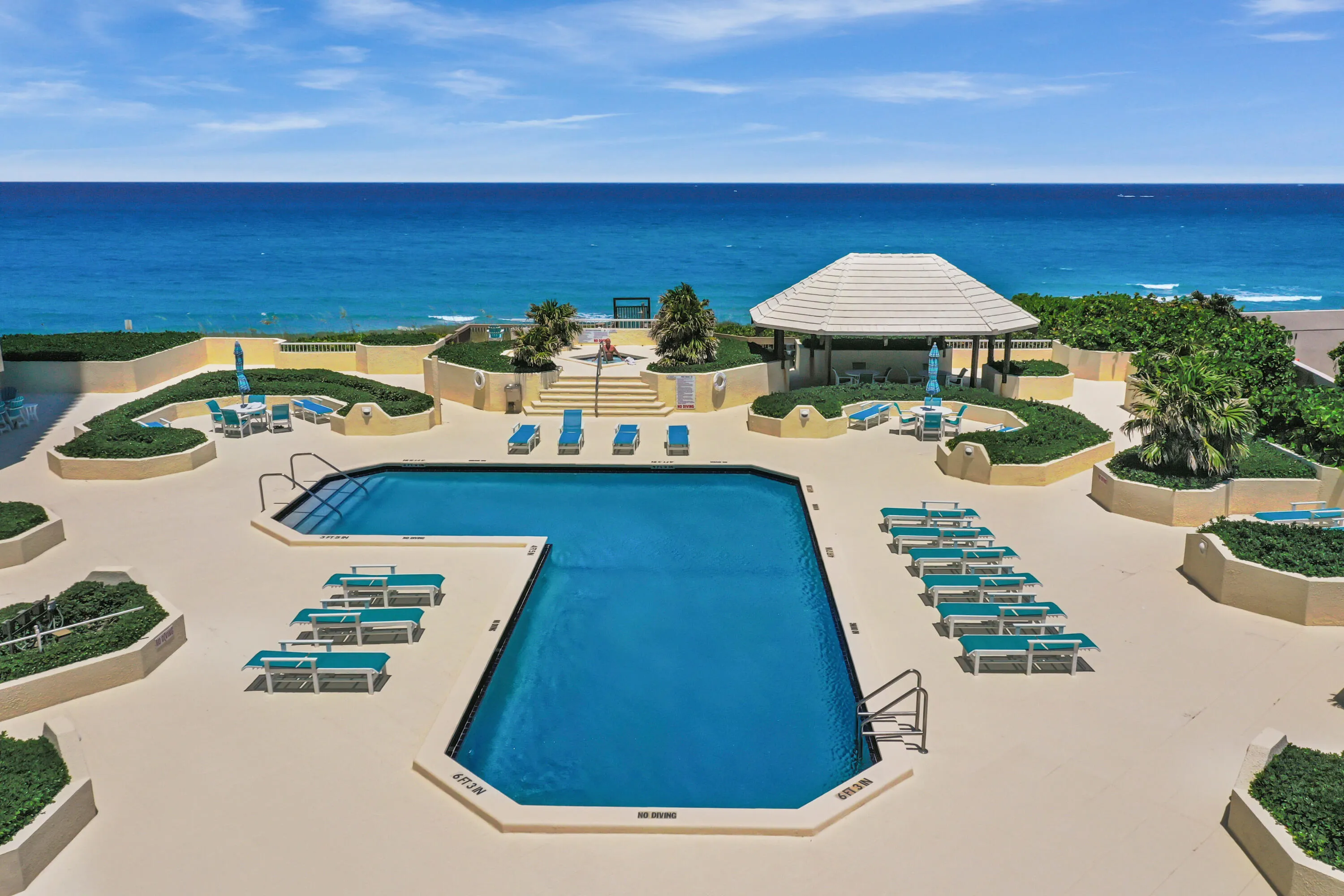 Expansive outdoor pool area featuring a rectangular swimming pool, a shaded gazebo, and elevated planted beds