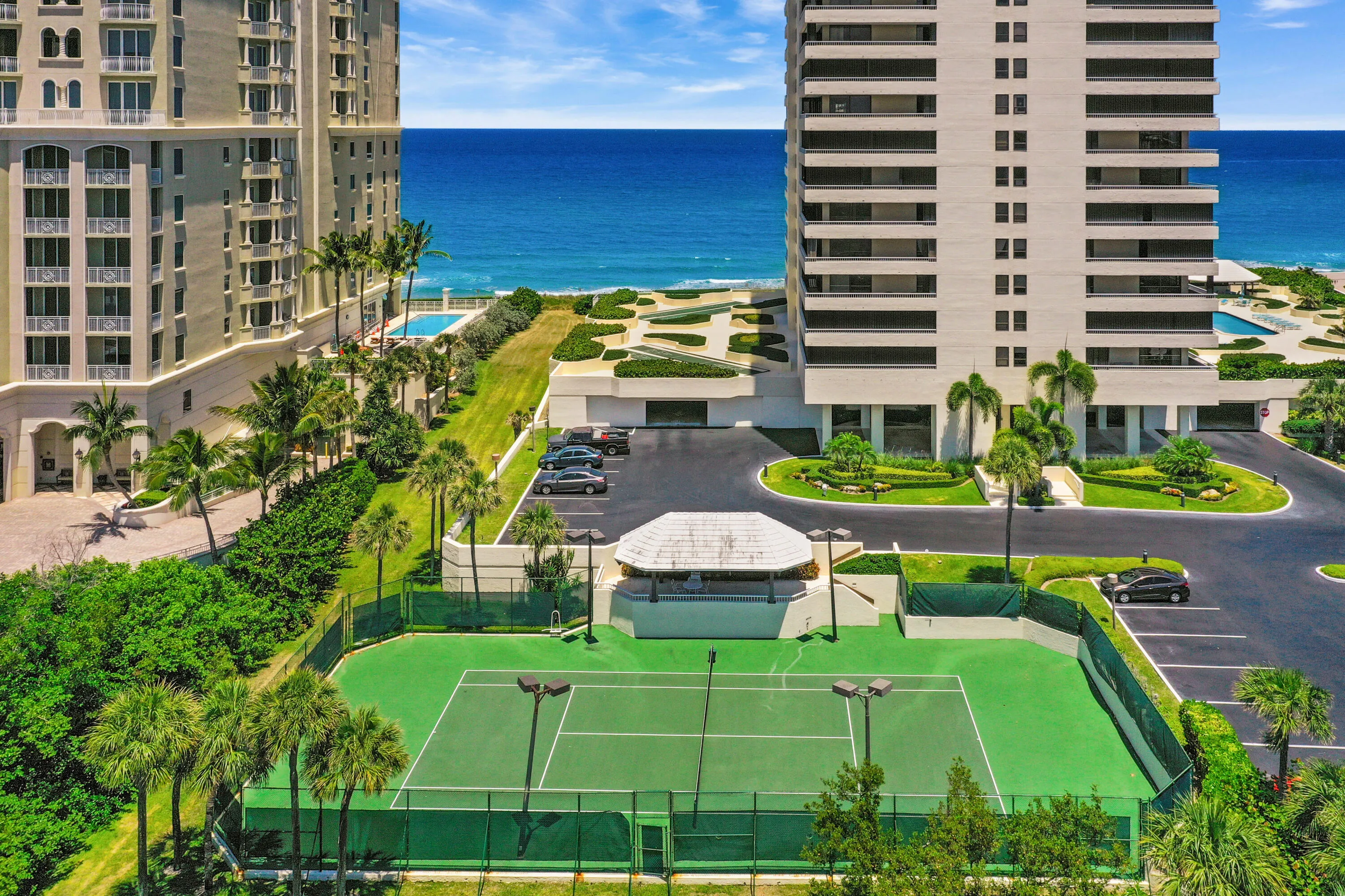 Oceanfront property featuring two multi-story buildings, a tennis court, a swimming pool, and landscaped grounds