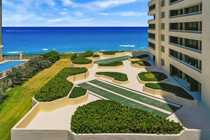Oceanfront property featuring multiple shuffleboard courts, manicured hedges, a structured building exterior with balconies, and an outdoor swimming pool