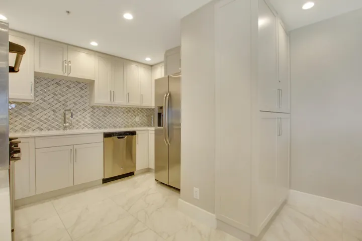 Kitchen featuring white cabinetry, stainless steel appliances, mosaic tile backsplash, recessed lighting, and large format floor tiles