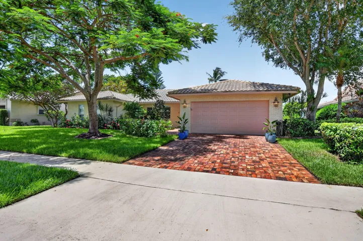 Tiled roof residence with a paver driveway, mature trees, and manicured landscaping