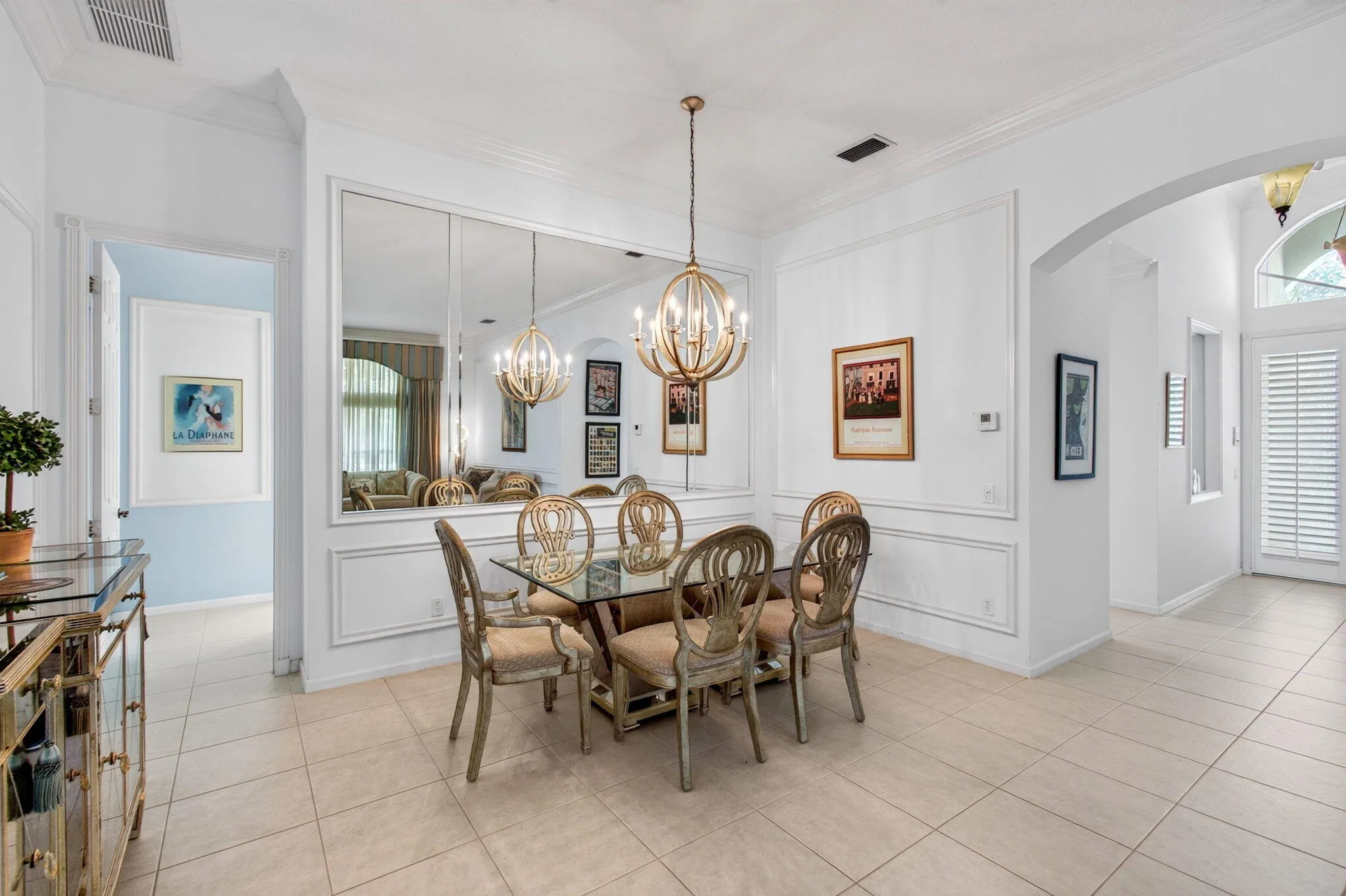 Tile flooring, mirrored wall paneling, decorative wainscoting, arched entryway, and a prominent chandelier