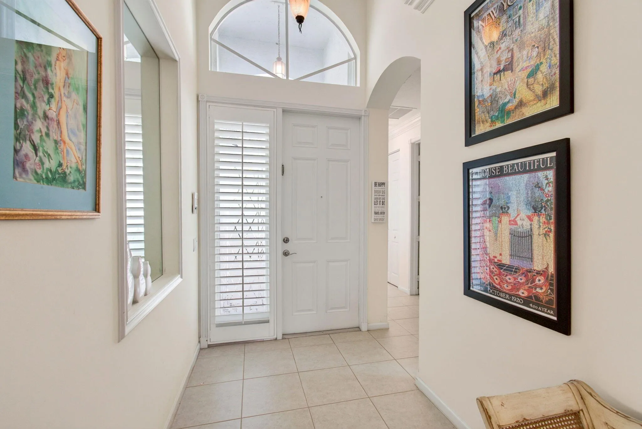 Arched transom window above a white paneled entry door with a sidelight, tiled flooring, and an arched hallway opening