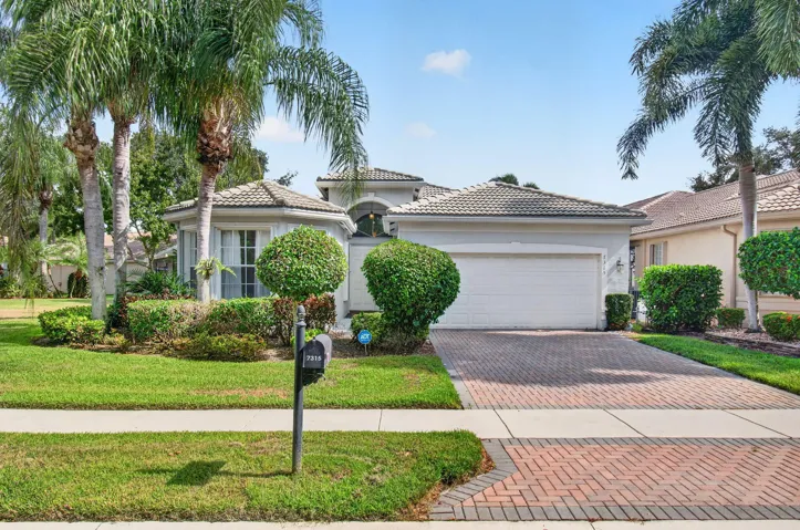 Stucco exterior with a tiled roof, mature palm trees, and a brick paver driveway