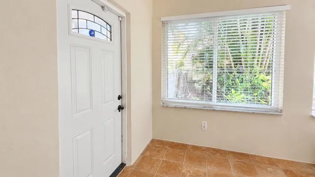 White paneled entry door with decorative glass transom, white window blinds, and tile flooring