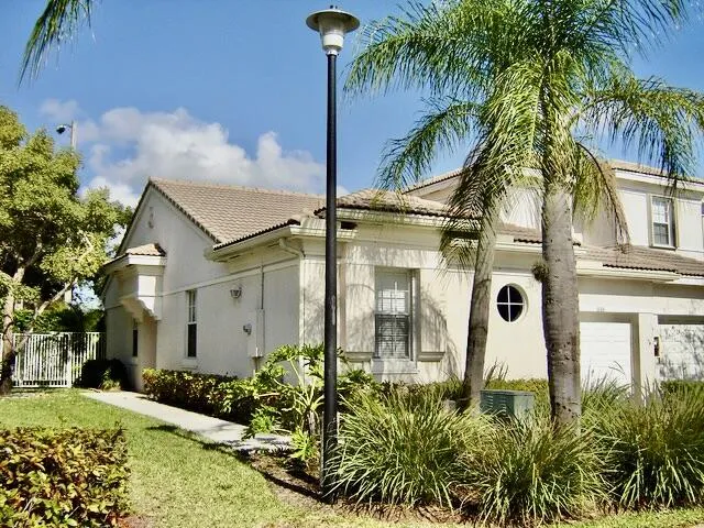 Stucco exterior with a tiled roof, featuring a circular window, an attached garage, and established landscaping