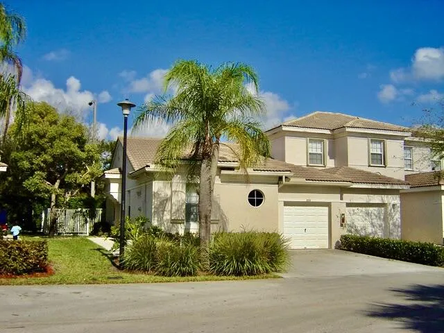 Stucco exterior with tile roofing, featuring a circular window, an attached two-car garage, and established landscaping