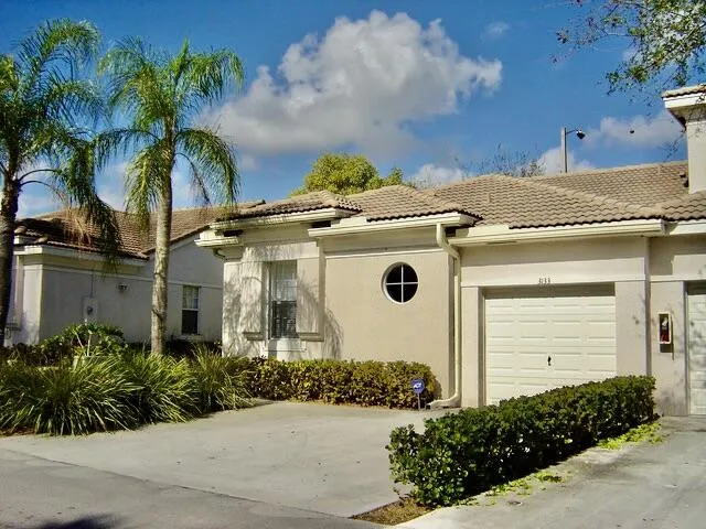 Stucco exterior with a tiled roof, integrated garage, and mature landscaping