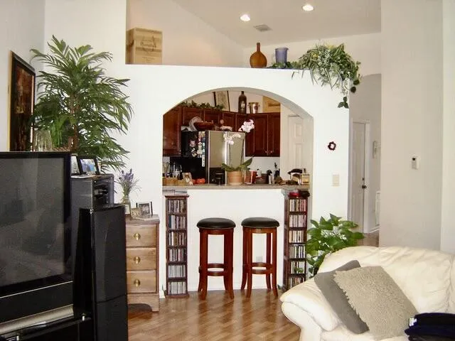 Arched pass-through to the kitchen with a breakfast bar, wood-finish flooring, recessed lighting, and a high ceiling