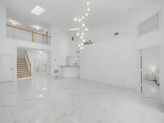 Expansive open floor plan showcasing polished stone flooring throughout, soaring ceilings with recessed and pendant lighting, and a floating staircase with wood-finish treads and metal railings