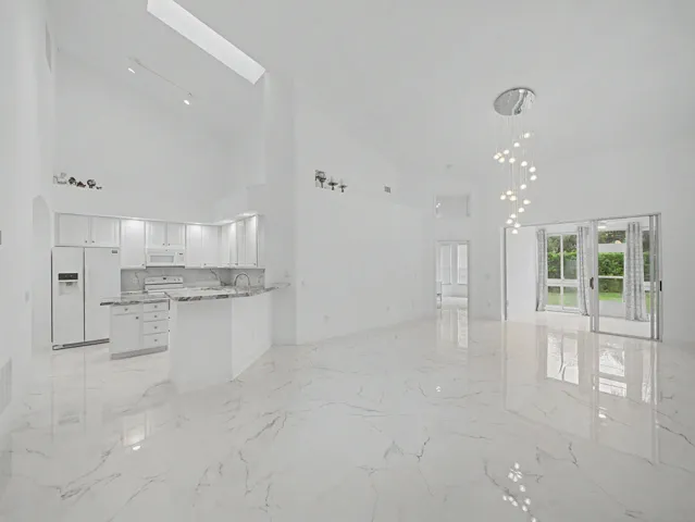 Vaulted ceilings, white kitchen cabinetry with light countertops, built-in breakfast bar, modern chandelier, and sliding glass doors