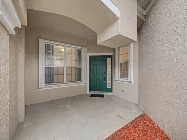 Welcoming covered entry featuring a decorative tile accent, dual multi-pane windows with white frames, and a dark green entry door with sidelights
