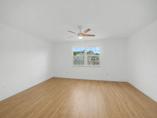 Bright, open bedroom showcasing gleaming wood-finish flooring, crisp white walls, and abundant natural light from dual windows