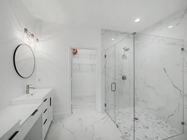 Glass-enclosed shower with a rainfall showerhead, tiled flooring, and marble-look wall tiling