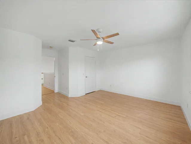 Spacious bedroom featuring wood-finish flooring, ceiling fan with integrated lighting, and abundant natural light from multiple windows