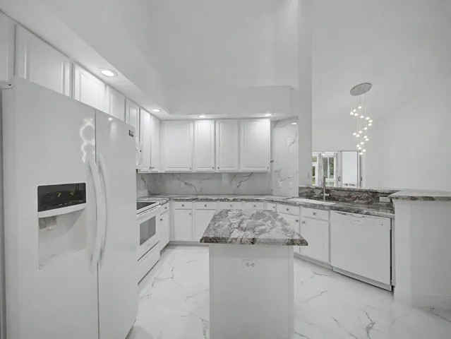 White shaker cabinetry, marble-look countertops, white appliances, and a central island with an integrated sink