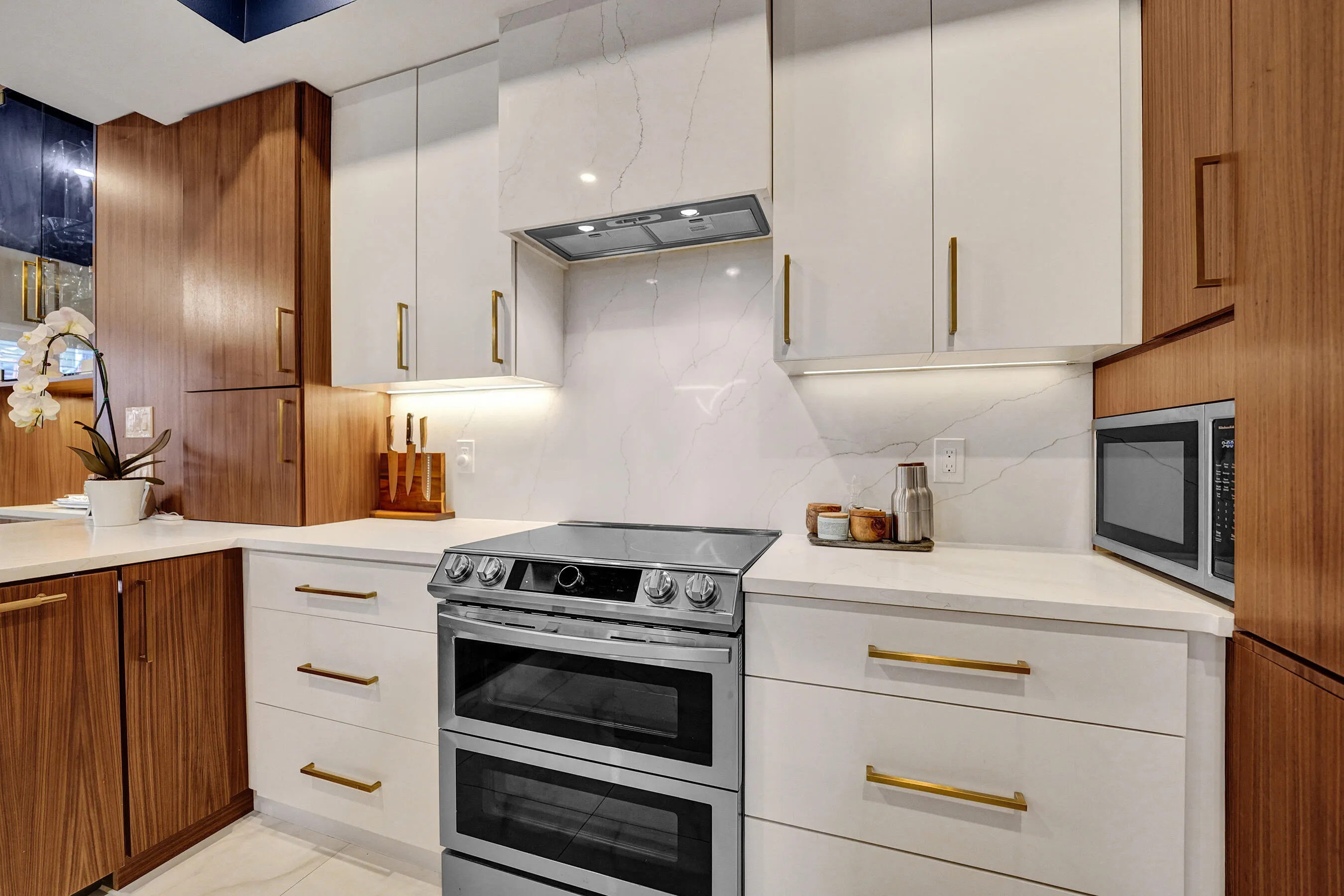 Two-tone kitchen cabinetry with wood-finish and white panels, white countertops, built-in stainless steel double oven range, and integrated microwave