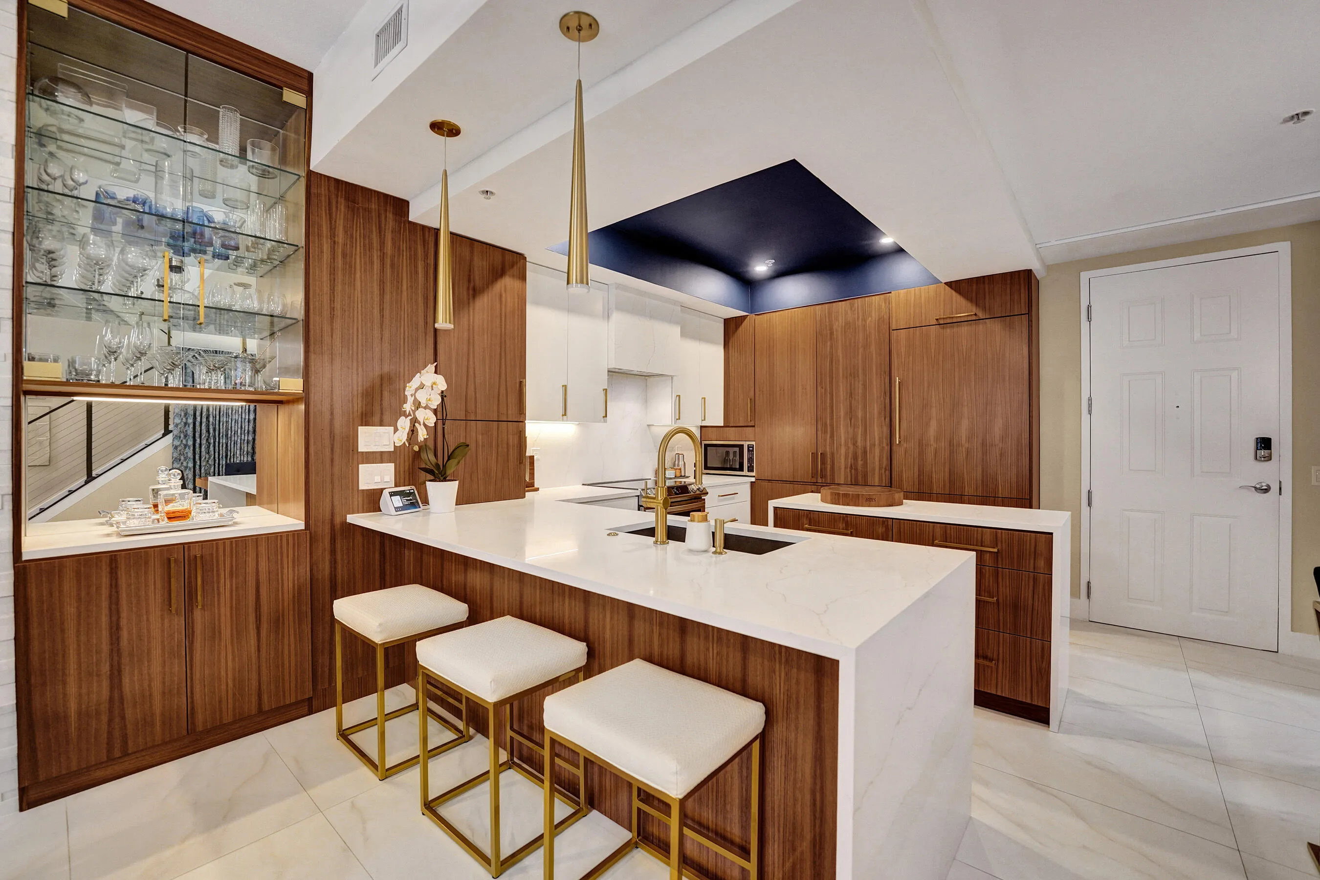 Kitchen featuring wood-finish cabinetry, a large center island with a light-toned countertop, integrated appliances, and a built-in display cabinet with glass shelving