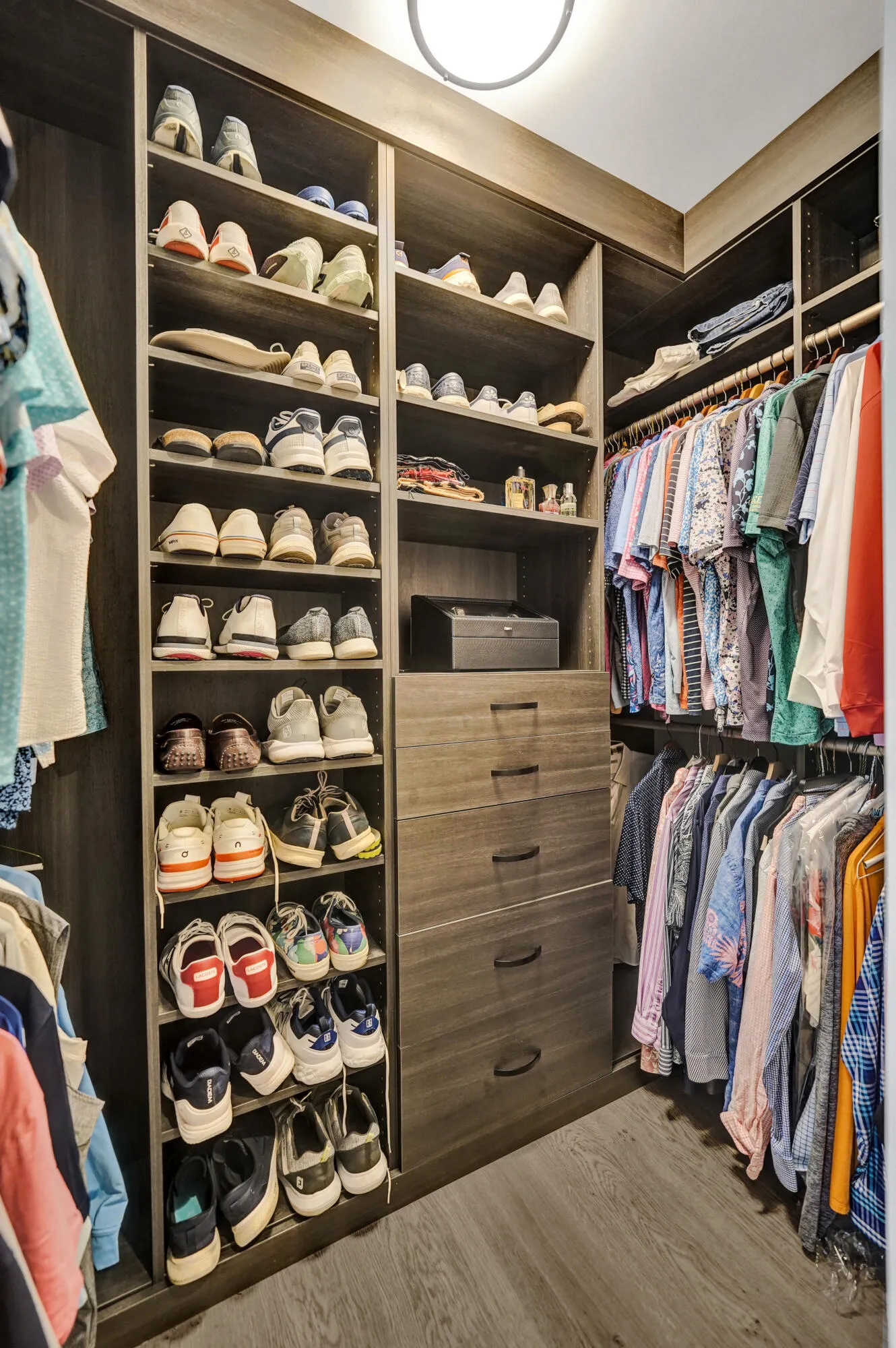 Built-in closet system featuring wood-finish cabinetry, multiple shelving units, integrated drawers, and hanging rods